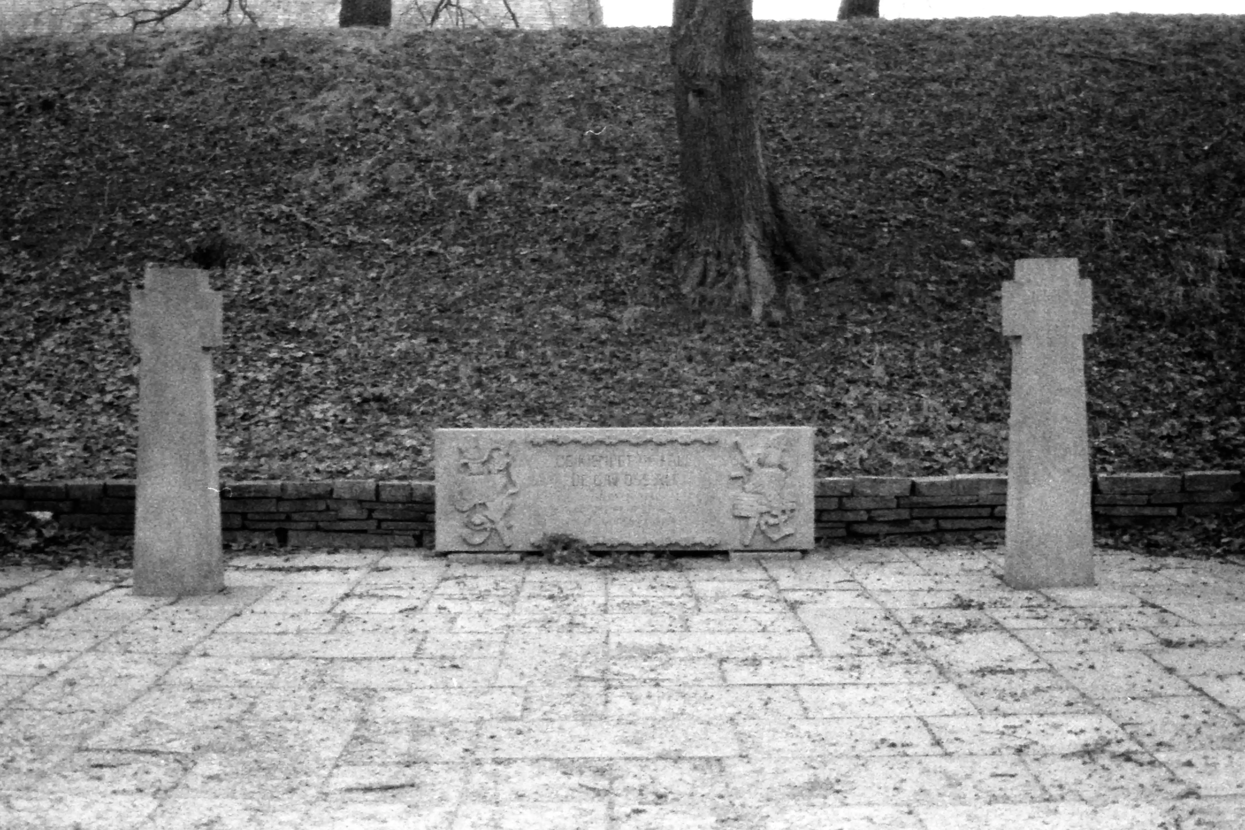 Black and white picture of a gravestone surrounded by two stone crosses. The text on the stone is unintelligble