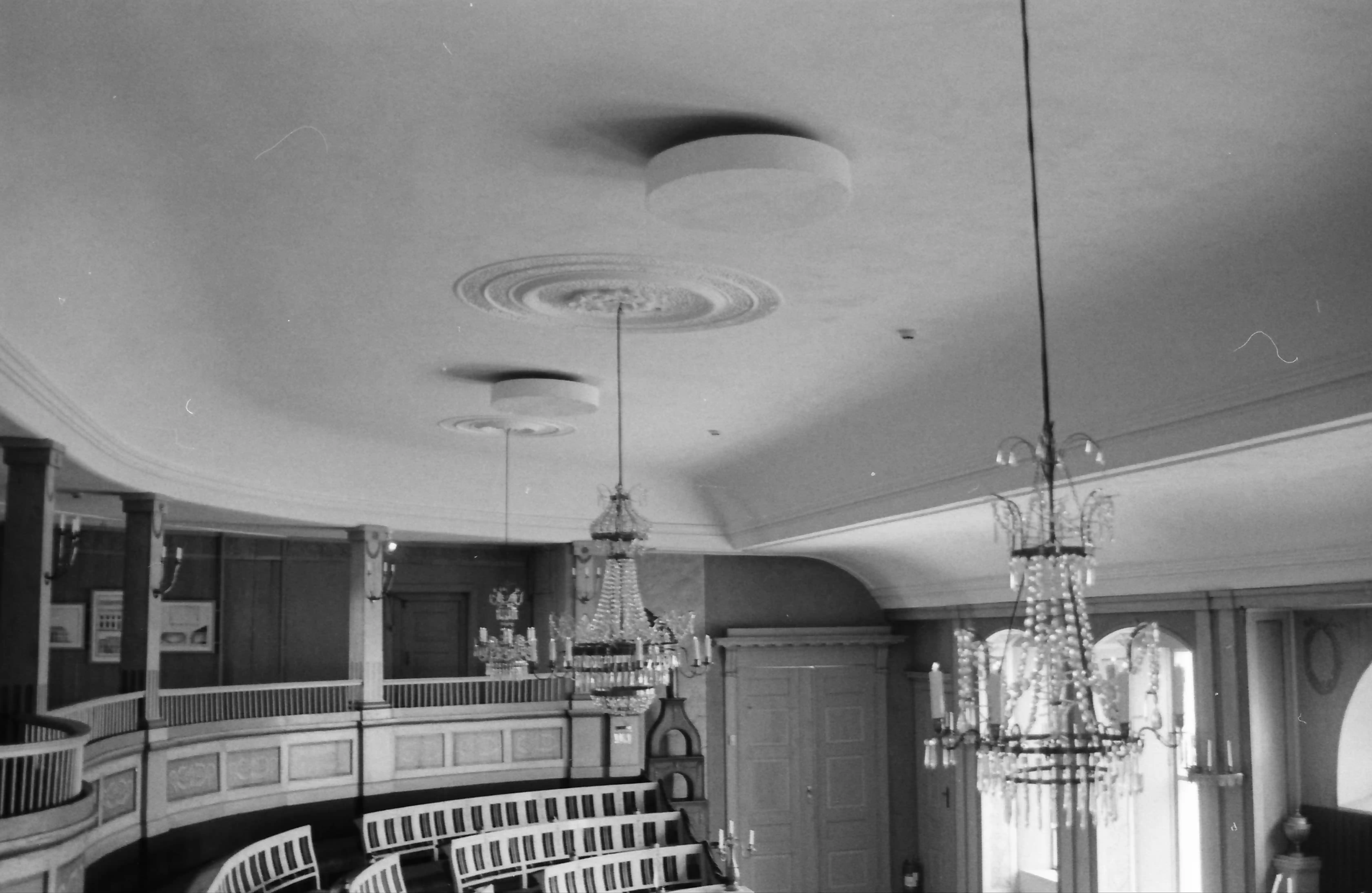Black and white picture of a formal hall of some sort, focusing on its chandeliers